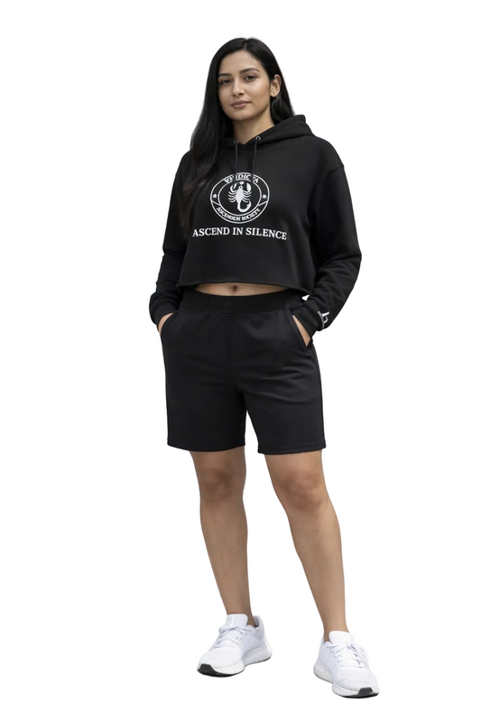 Person wearing a black hoodie and shorts standing on steps with a gray wall background