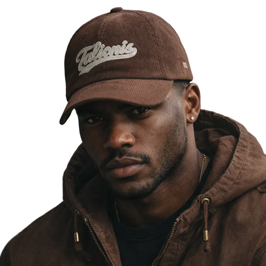 Man wearing a brown cap and jacket with 'Talib Kweli' branding against a neutral background