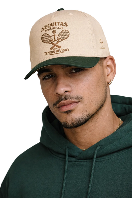Man wearing a beige cap with 'Acquitas Athletic Club' logo and green hoodie against a gray background