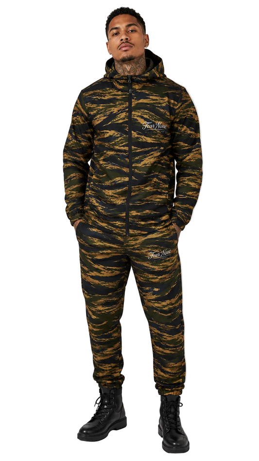 A man modeling a tiger stripe camouflage hooded zip-up jacket and matching jogger pants set. The set features a black and brown tiger stripe pattern with white 'The Real Deal' brand logo on the chest and thigh.