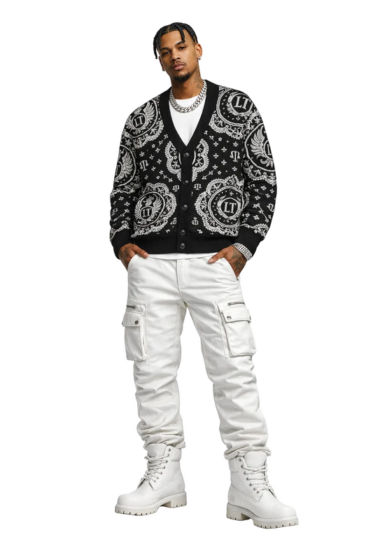 Man wearing a black and white patterned cardigan with white pants and boots on a white background