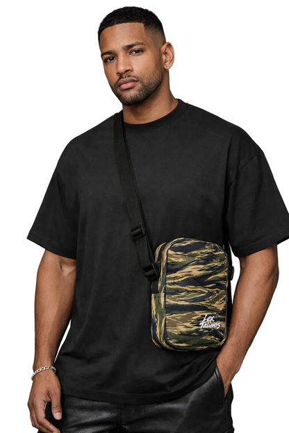 Man wearing a black t-shirt with a camouflage crossbody bag on a gray background