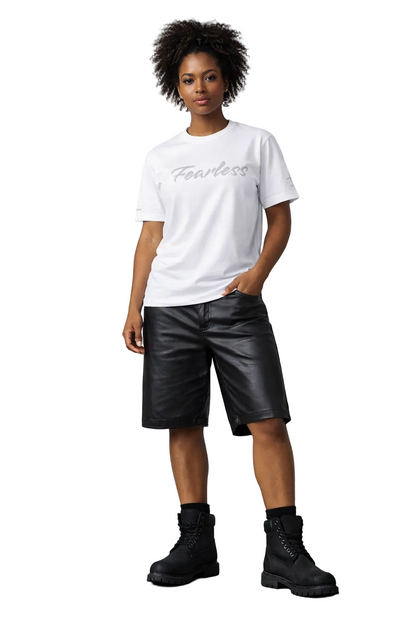 Person wearing a white t-shirt with 'Fearless' text, black leather shorts, and black boots on a gray background