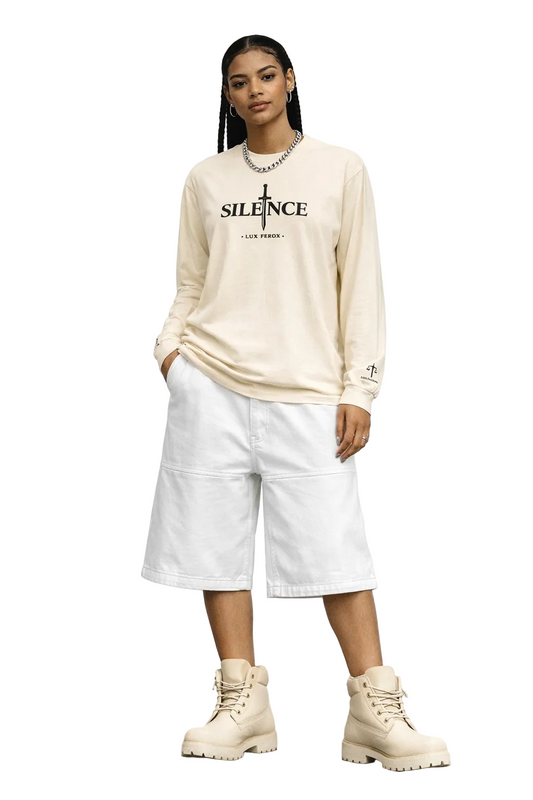 Person wearing a beige long-sleeve shirt with text and white pants against a plain background