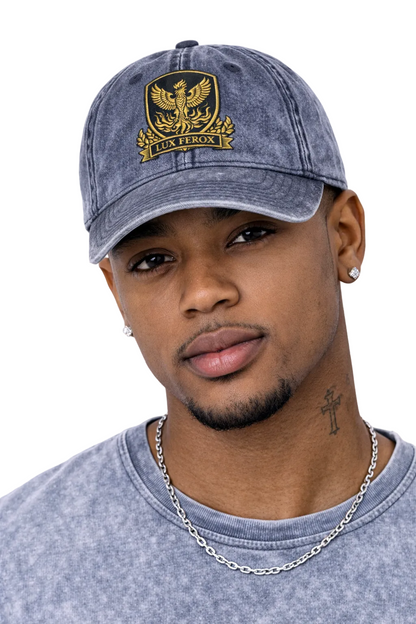 Man wearing a denim cap with an emblem and gray shirt against a white background
