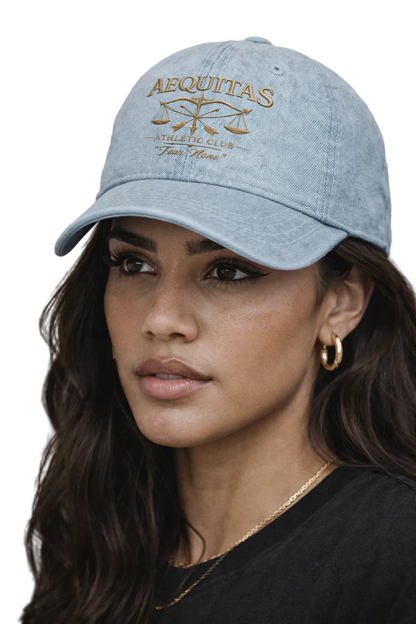 Woman wearing a light blue cap with 'AEQUITAS' branding against a neutral background