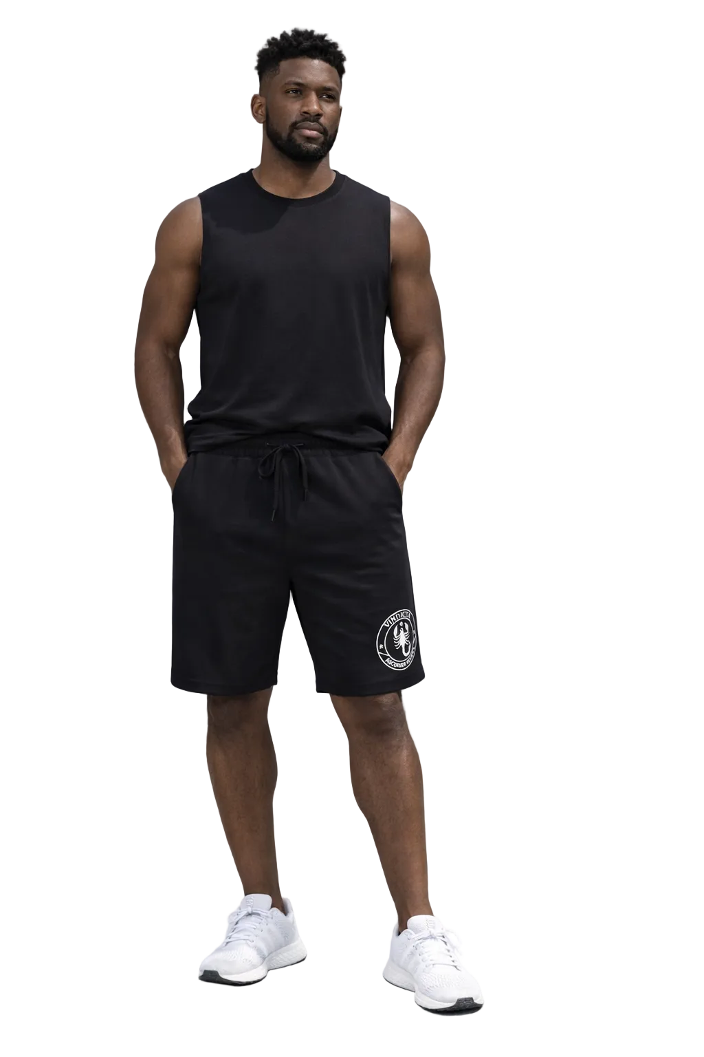 Man wearing a black sleeveless shirt and shorts with a logo, standing in front of a gray concrete wall.