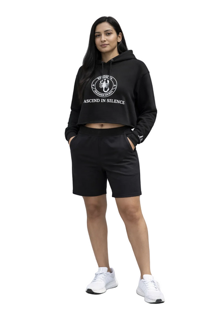 Person wearing a black hoodie and shorts standing on steps with a gray wall background