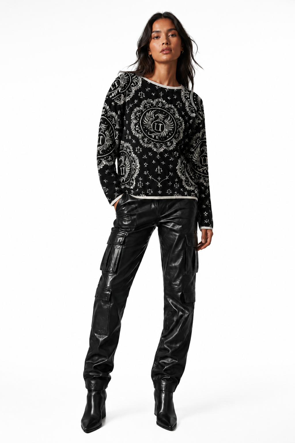 A model wearing a black and white ornate patterned long-sleeve top paired with black faux-leather cargo pants and black pointed boots, photographed against a solid white studio background.
