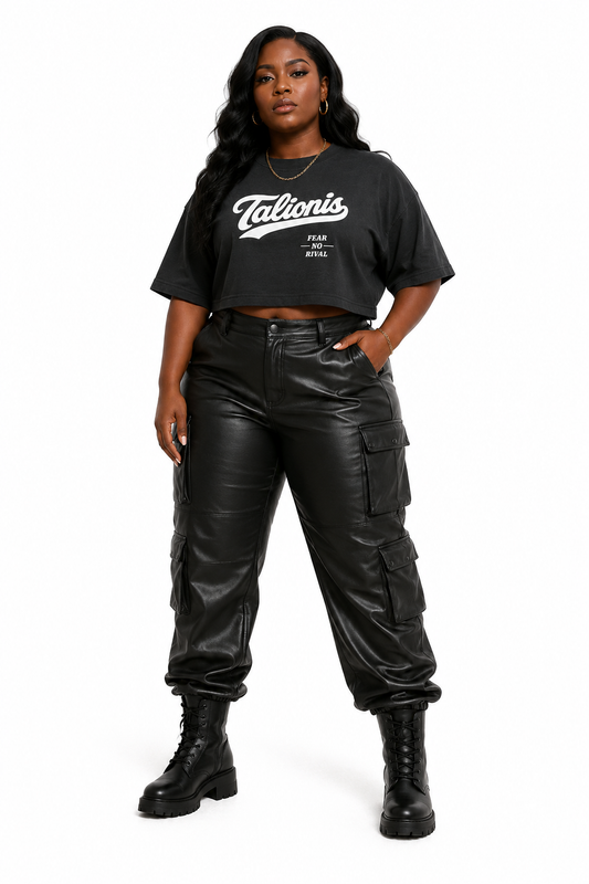 A woman modeling a black cropped graphic T-shirt and black faux-leather cargo pants with black combat boots, standing against a plain white studio background.