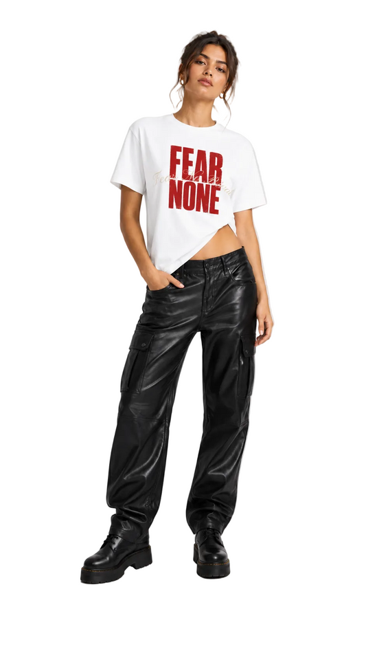 A model stands against a light gray studio background wearing a white cropped T-shirt with bold red text reading 'FEAR NONE' and black wide-leg pants with a glossy finish and black boots.