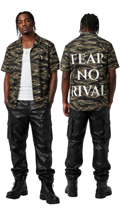 A model shown from the front and back wearing a Fear of God camo short-sleeve button-up shirt with 'FEAR NO RIVAL' printed in white on the back, paired with black cargo pants and black boots, against a light gray studio background.