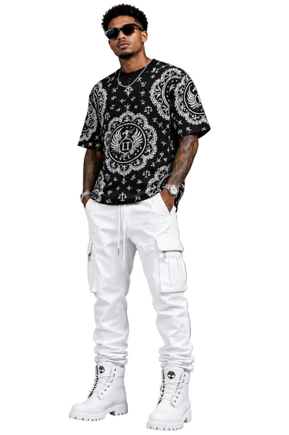 Man wearing a black patterned shirt, white pants, and white boots against a gray background