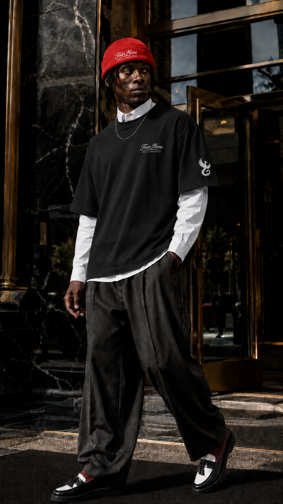 Lex Talionis editorial: layered black Fear None tee, white shirt and red beanie outside a marble entrance.
