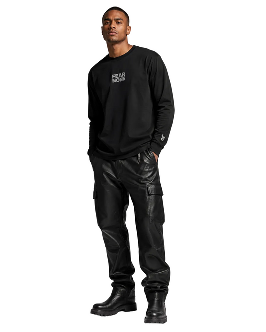 A man modeling a black long-sleeve crewneck sweatshirt with 'FEAR NONE' printed in white on the chest, paired with black cargo pants and black boots, against a solid gray studio background.