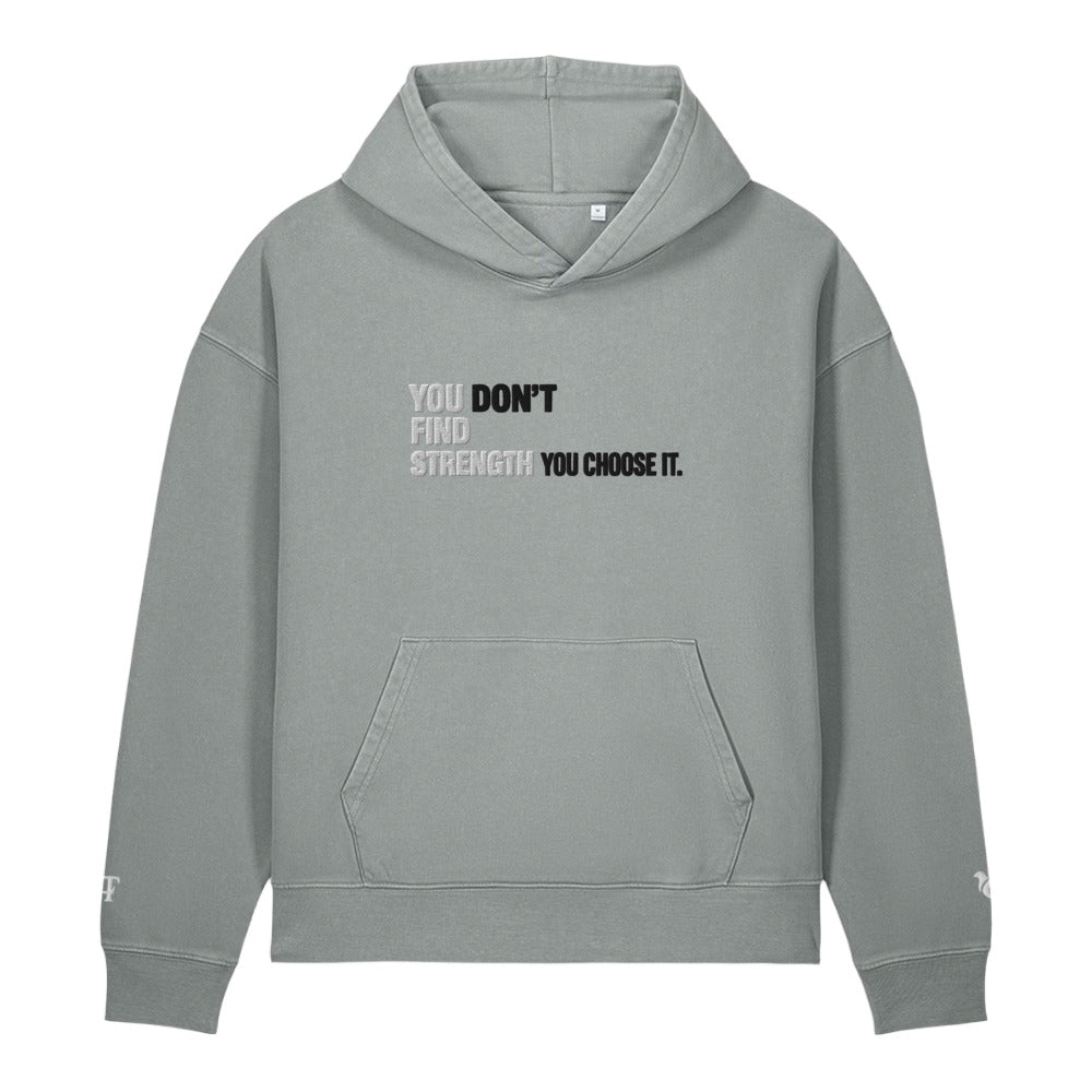A light gray pullover hoodie with a front kangaroo pocket and a motivational text graphic on the chest reading 'YOU DON'T FIND STRENGTH YOU CHOOSE IT.' in black and white, shown on a plain white background.