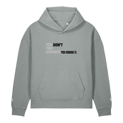 A light gray pullover hoodie with a front kangaroo pocket and a motivational text graphic on the chest reading 'YOU DON'T FIND STRENGTH YOU CHOOSE IT.' in black and white, shown on a plain white background.