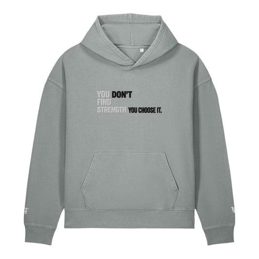 A light gray pullover hoodie with a front kangaroo pocket and a motivational text graphic on the chest reading 'YOU DON'T FIND STRENGTH YOU CHOOSE IT.' in black and white, shown on a plain white background.